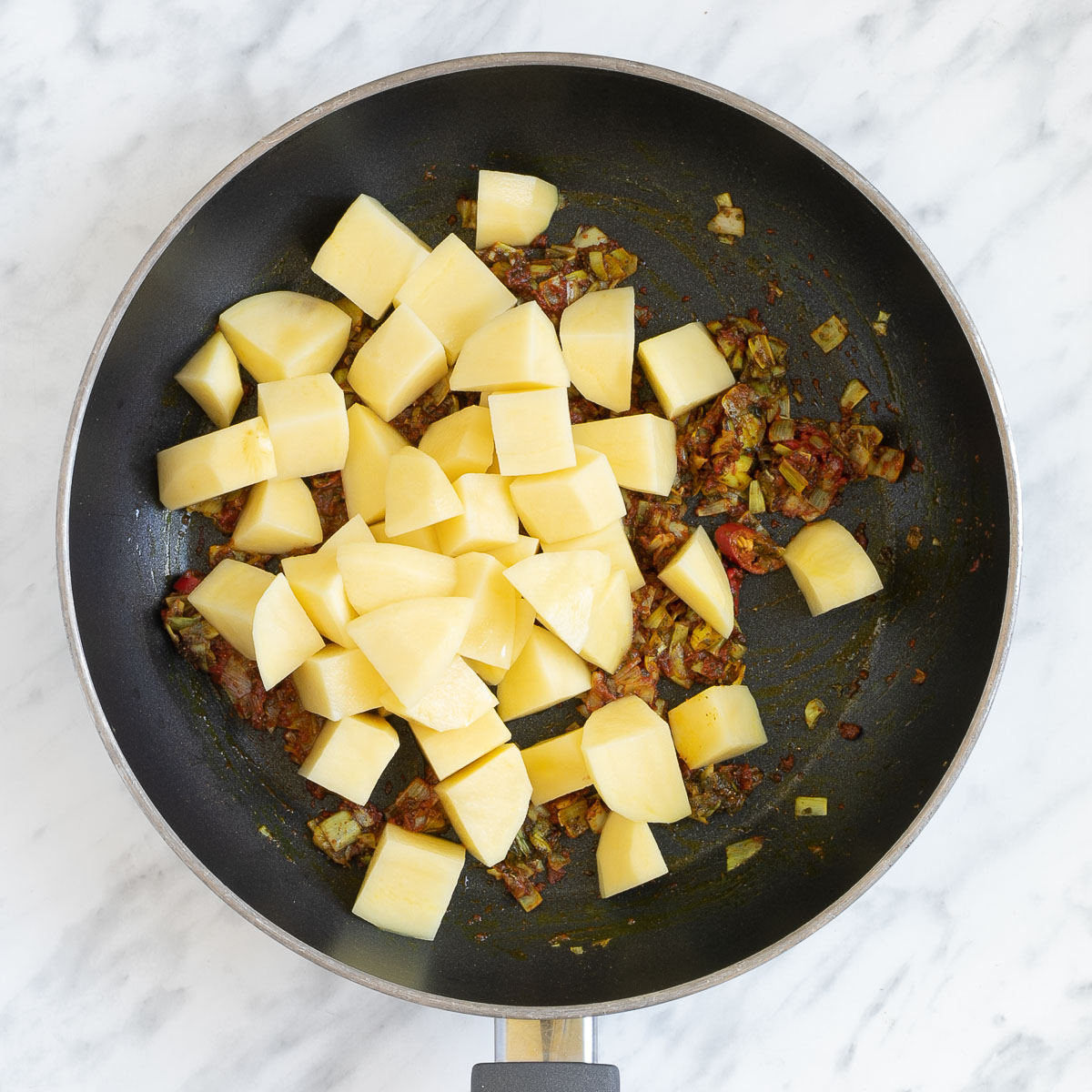Brown-orange sauteed onions with a large heap of raw diced potatoes in a frying pan.