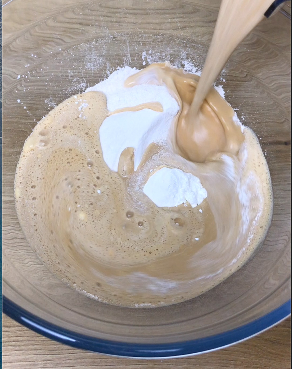 Glass bowl with white flour and a brownish-orange liquid is poured into it.