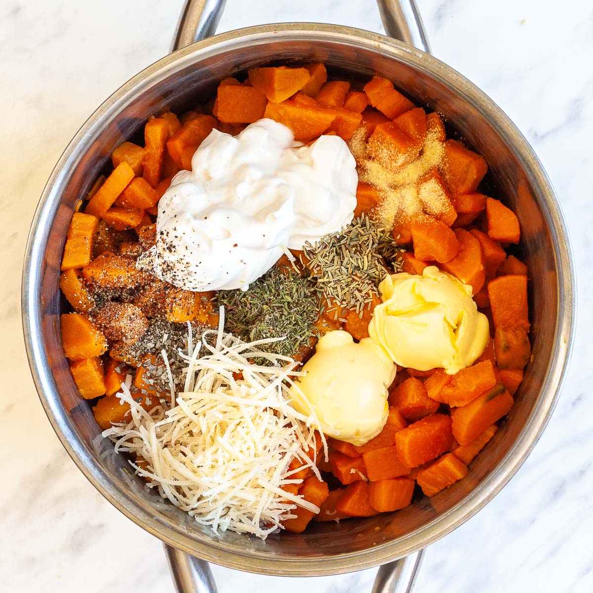 Stockpot with diced cooked orange sweet potatoes and heaps of shredded cheese, white cream, butter, and dried herbs.