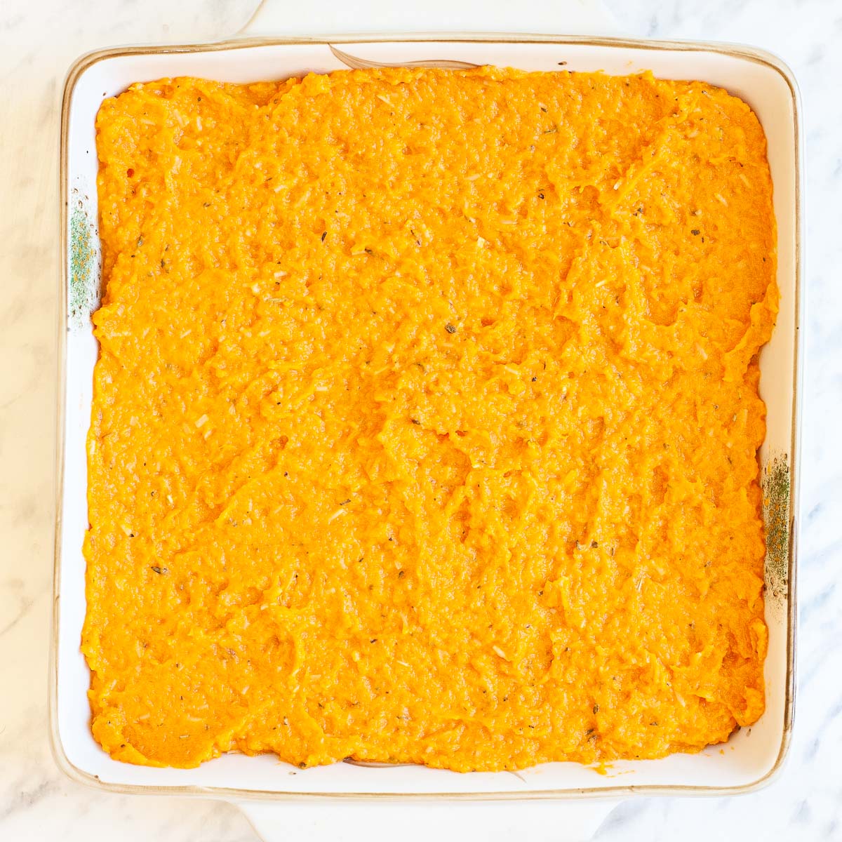 A white 9x9 baking dish with creamy mashed orange sweet potatoes.