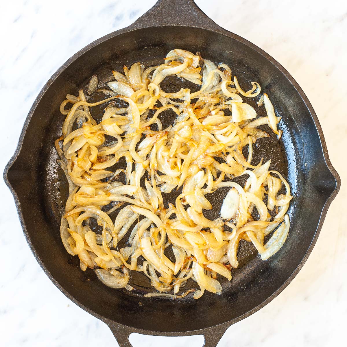 Black cast iron skillet with lightly brown caramelized onion slices.