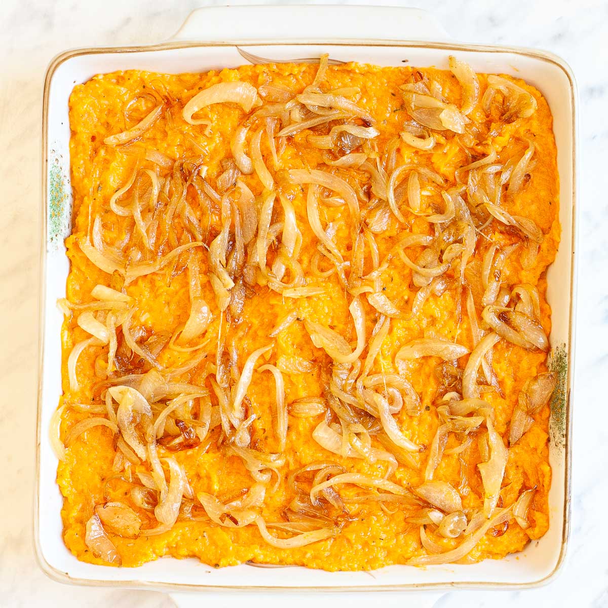 A white 9x9 baking dish with creamy mashed orange sweet potatoes topped with light brown caramelized onion slices.