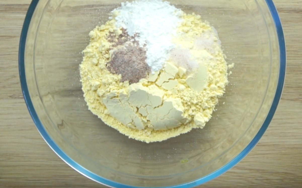 Glass bowl with yellow flour, white cornstarch, salt, and brown flakes.
