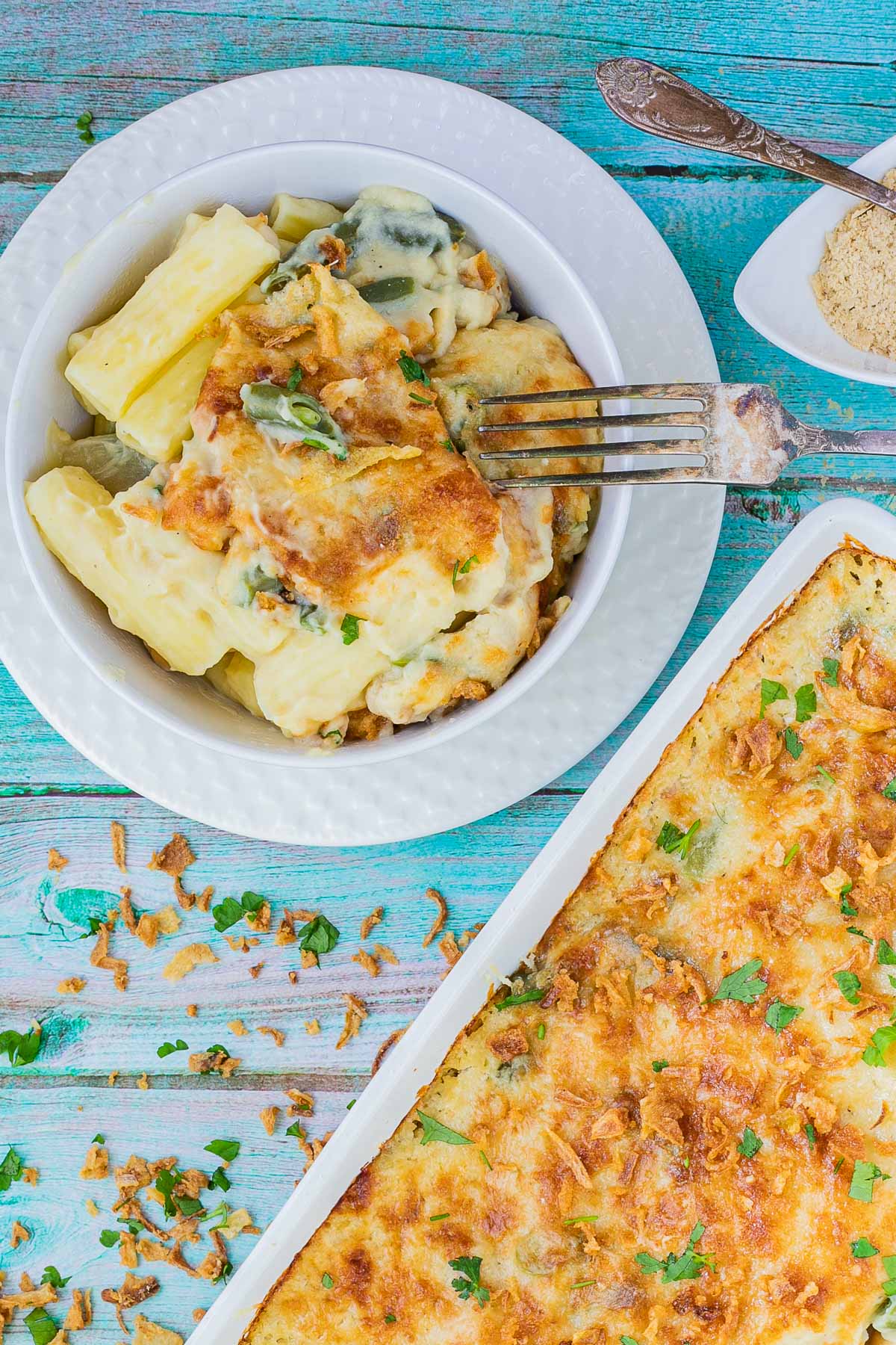 A small plate with penne pasta in creamy sauce, chickpeas and green peas topped with breadcrumbs and freshly chopped herbs.