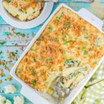 A baking dish with penne pasta in creamy sauce, chickpeas and green peas topped with breadcrumbs and freshly chopped herbs. The corner part is missing and served in a small plate on the side.