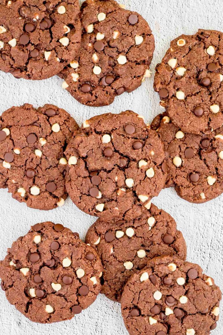 Dark brown cookies with white and dark chocolate chips on a white surface.