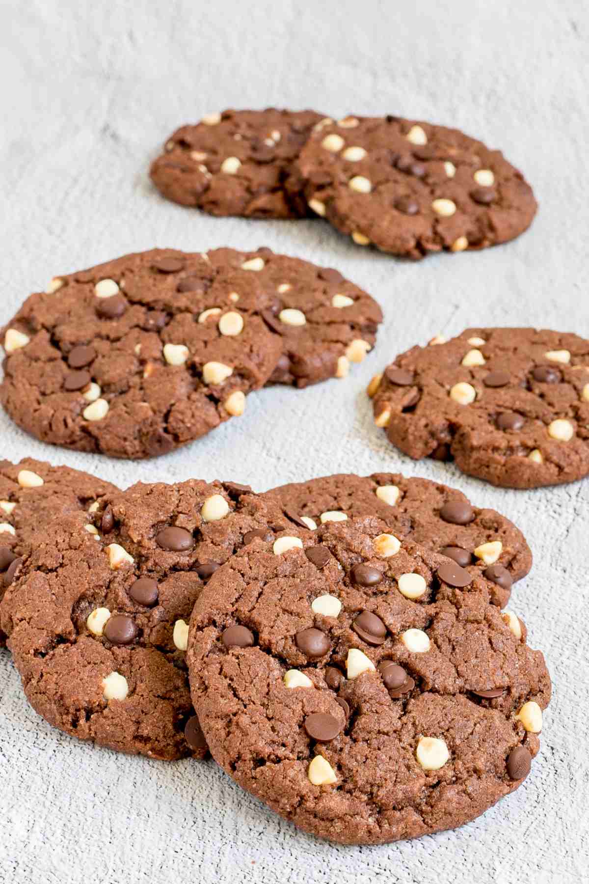 Dark brown cookies with white and dark chocolate chips on a white surface.