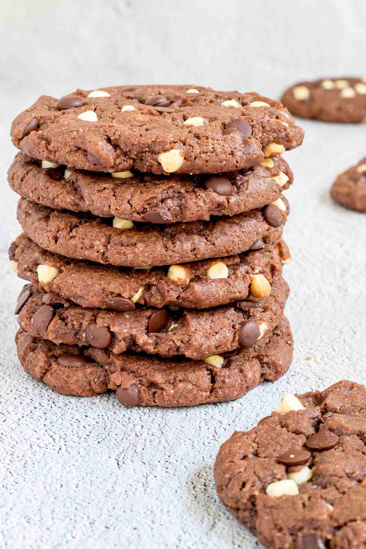 A stack of dark brown cookies with white and dark chocolate chips on a white surface.