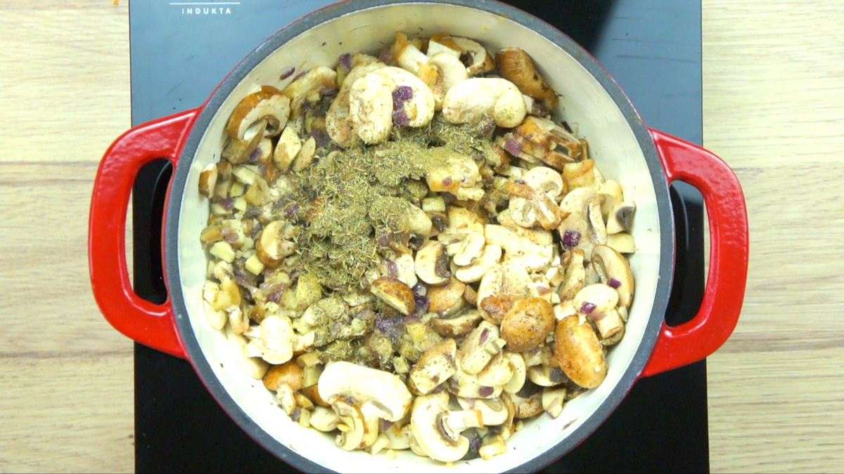 Red-white enameled Dutch oven with lots of sliced mushrooms and heaps of dried herbs.