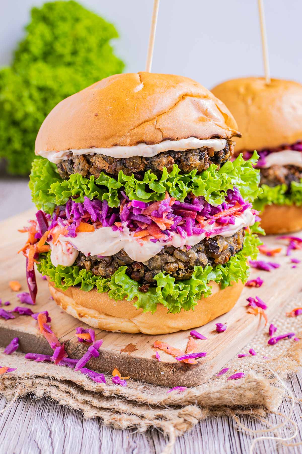 A burger bun with raffled green lettuce two lentil patties, purple coleslaw and light orange sauce. 