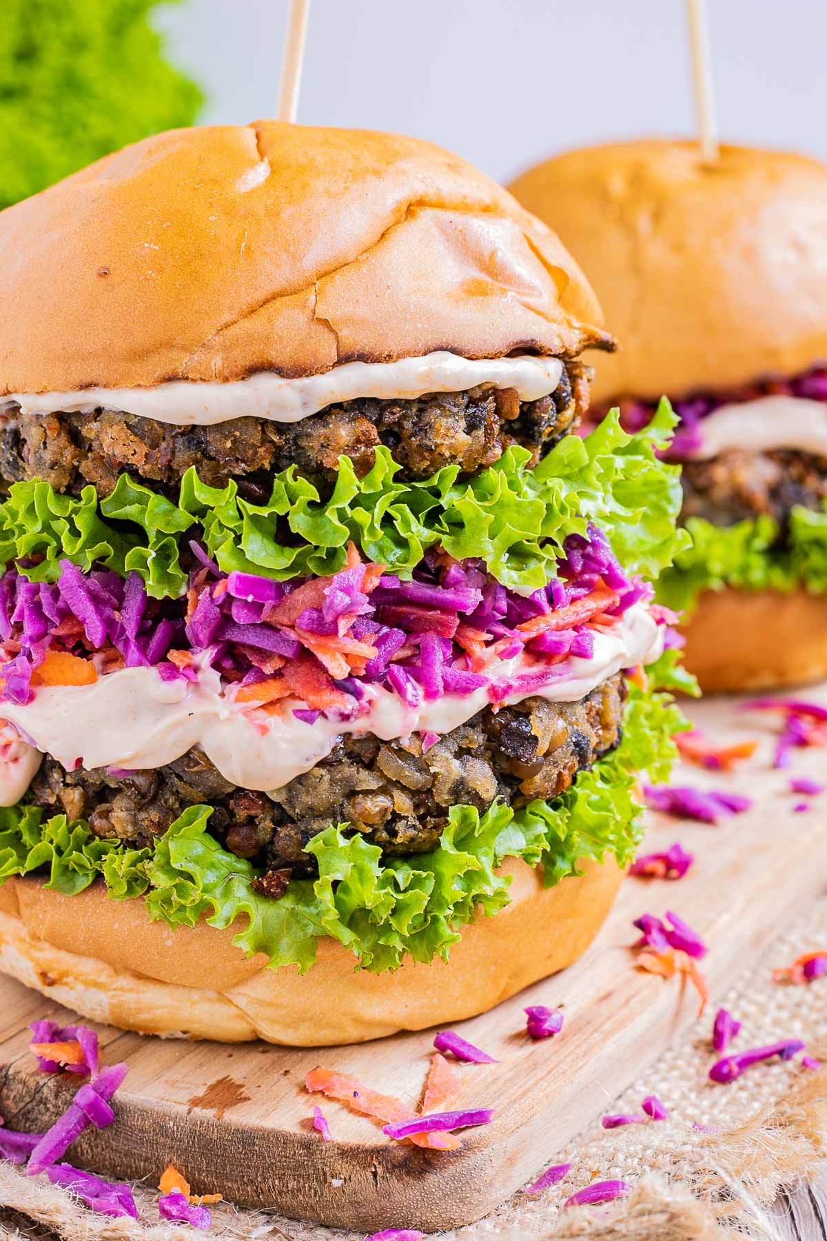 A burger bun with raffled green lettuce two lentil patties, purple coleslaw and light orange sauce.