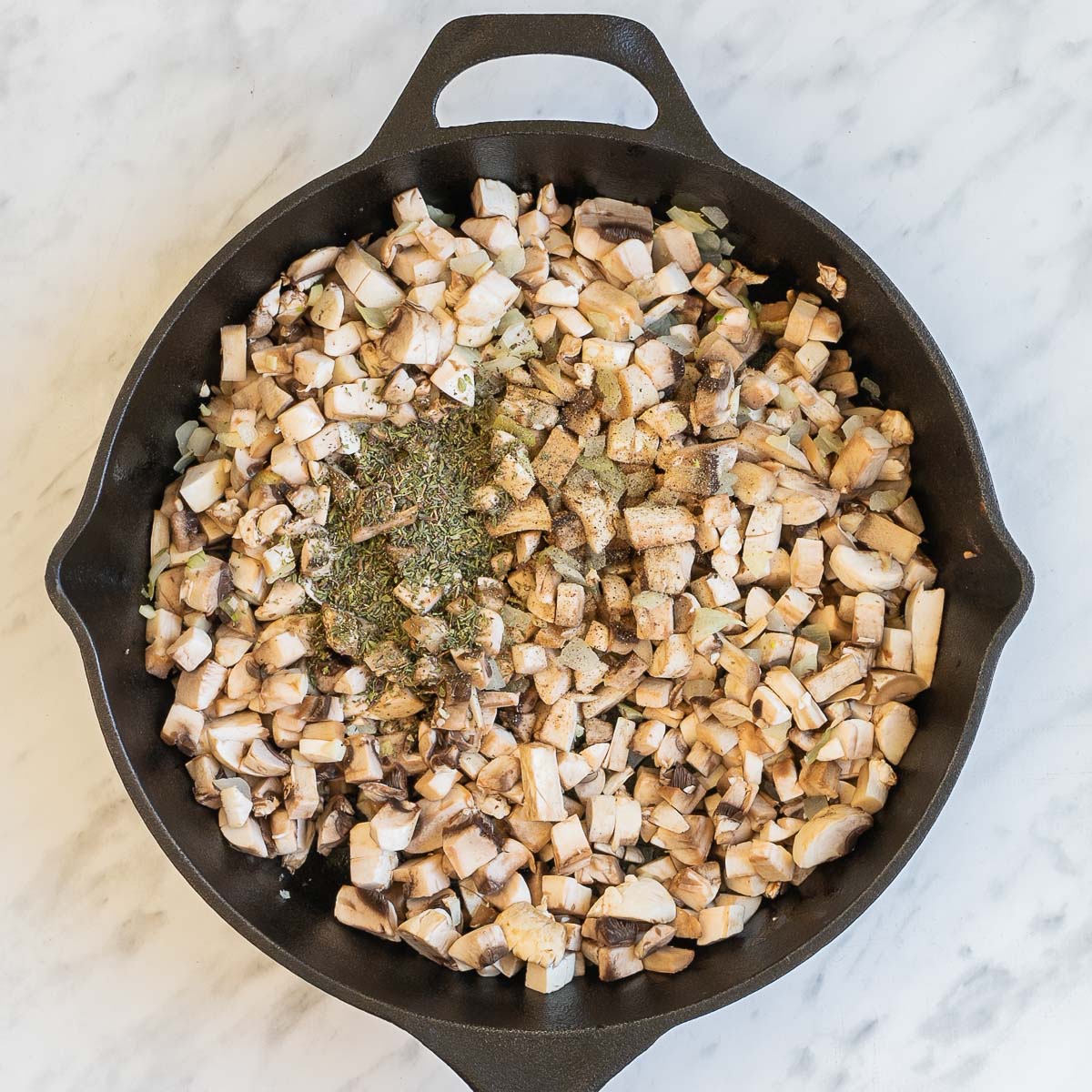 Cast iron skillet with chopped mushrooms and dried herbs.