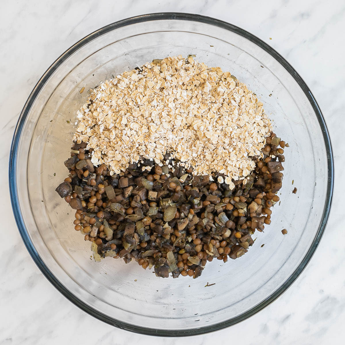 A glass bowl with the sauteed mushrooms and lentils with a heap of oats.