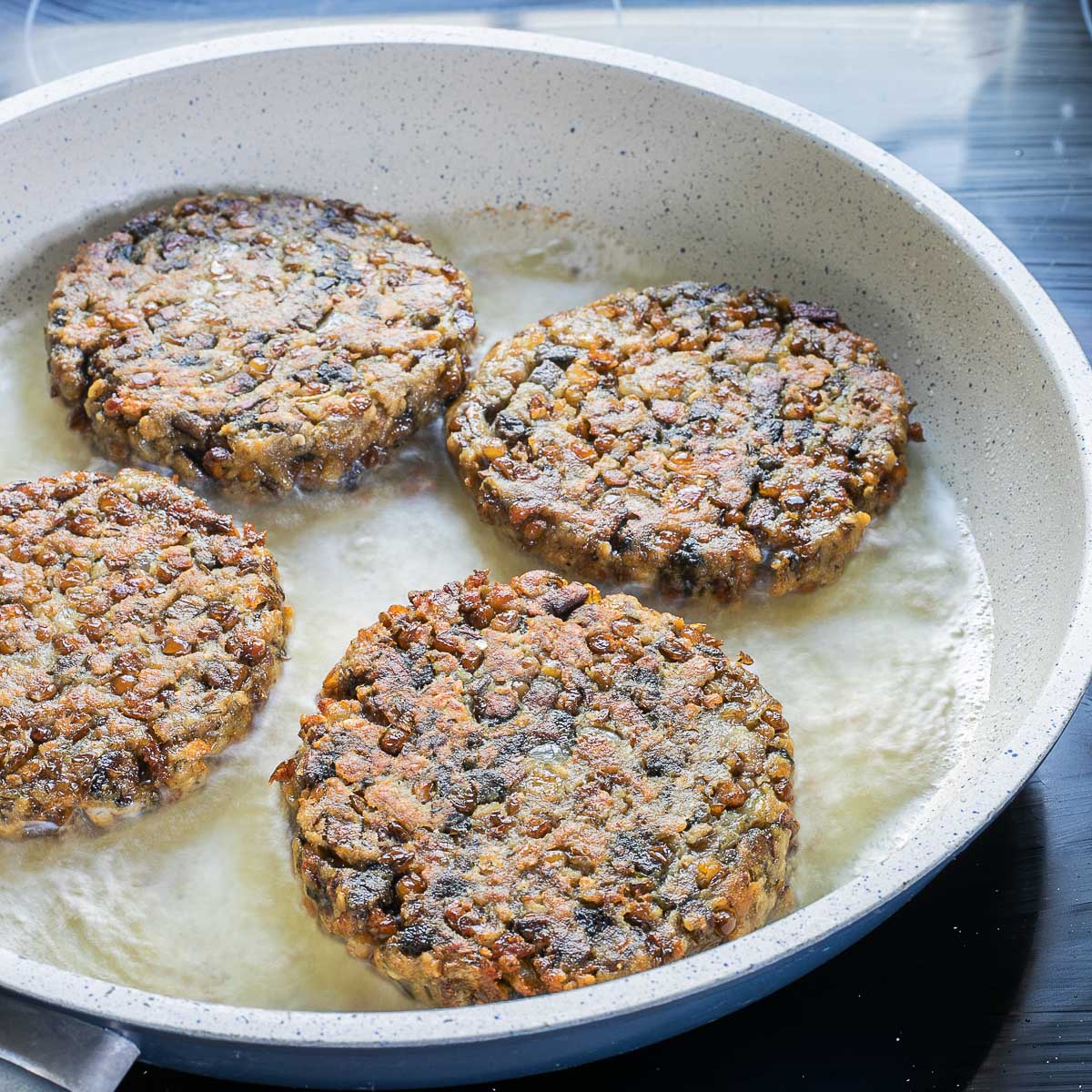 4 crispy lentil patties in a frying pan with bubbly oil just after they were turned.