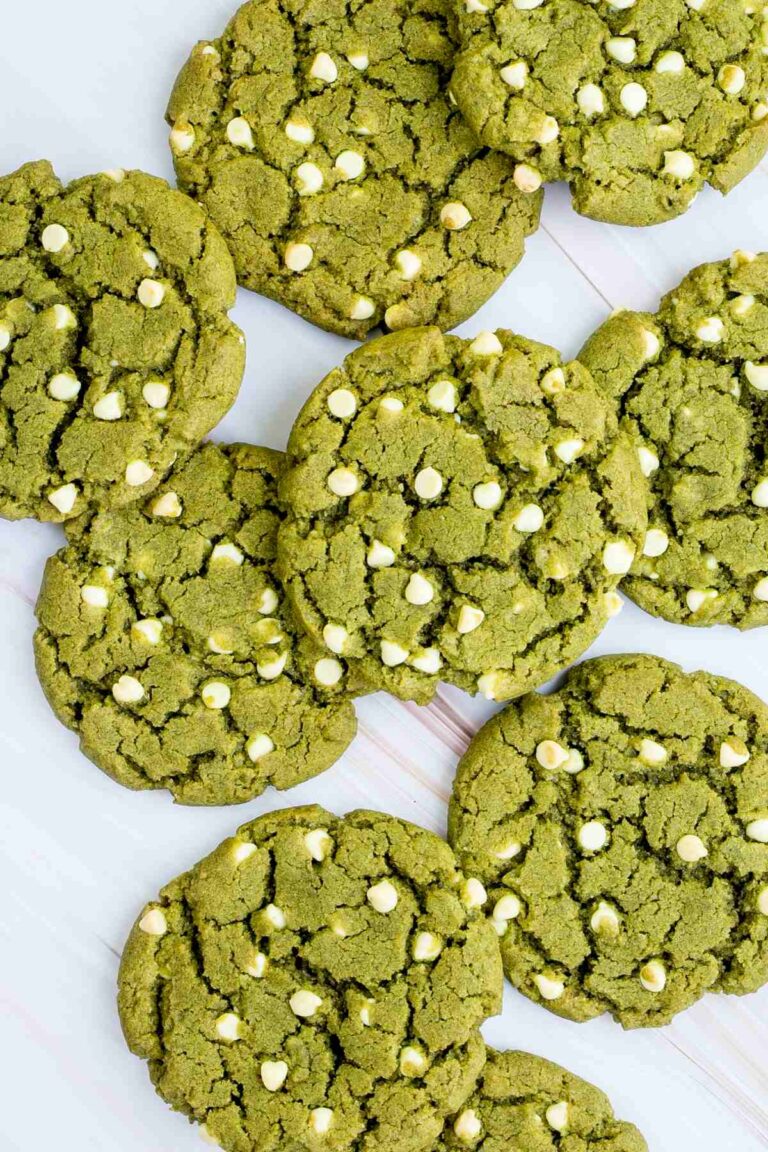 Lots of vibrant green cookies with white chocolate chips on a marble surface.