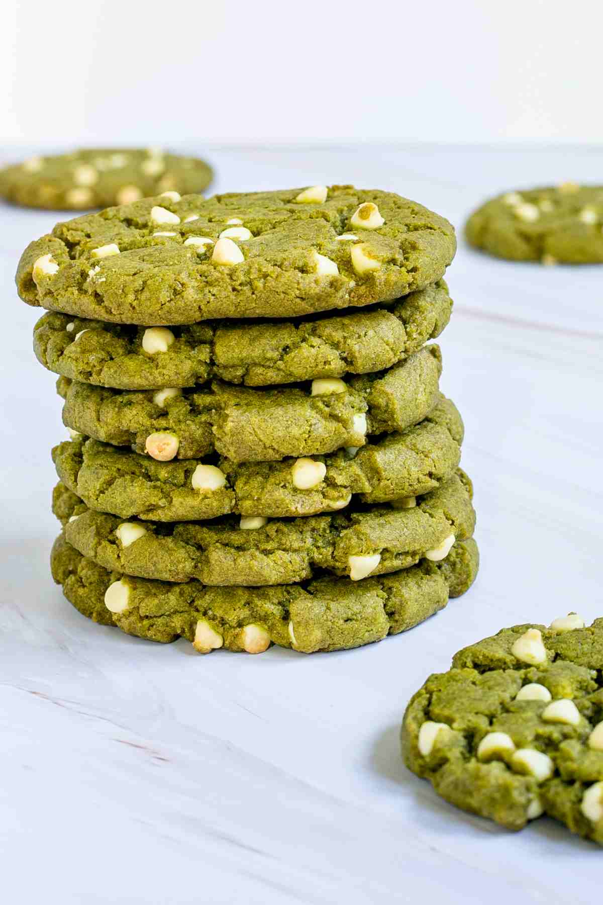 A stack of vibrant green cookies with white chocolate chips on a marble surface.