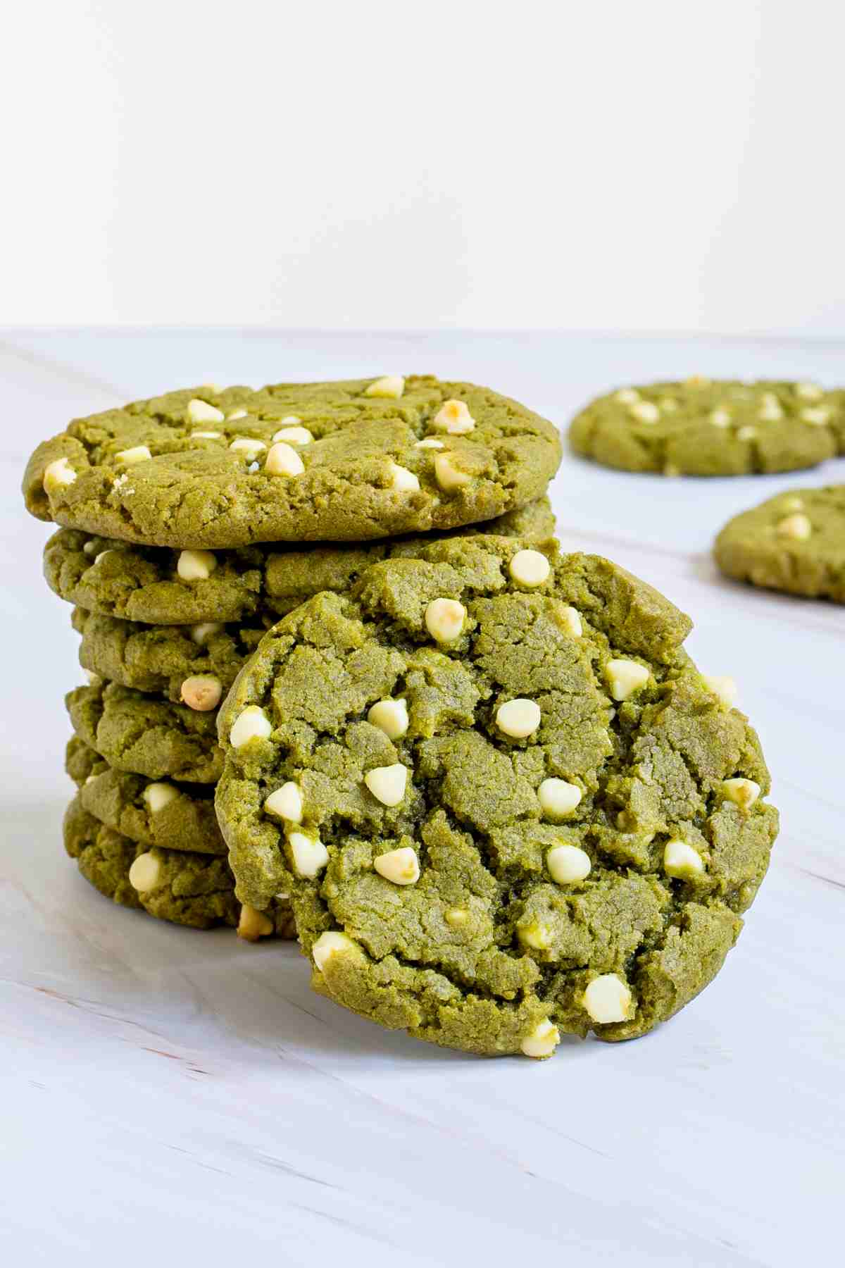 A stack of vibrant green cookies with white chocolate chips on a marble surface.
