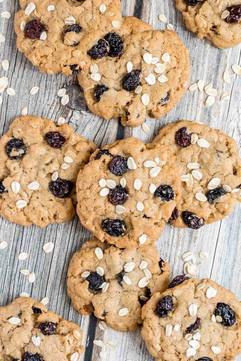 Lots of cookies with oats and raisins on a wooden surface. More oats are sprinkled around them.