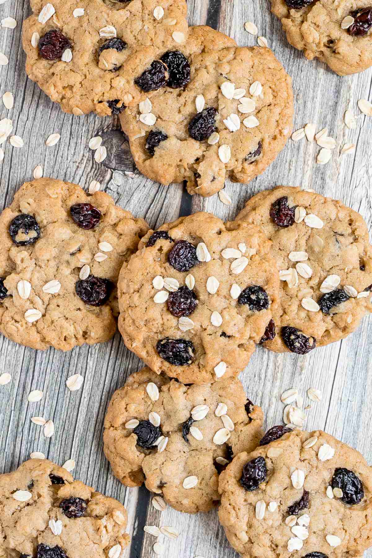 Lots of cookies with oats and raisins on a wooden surface. More oats are sprinkled around them.