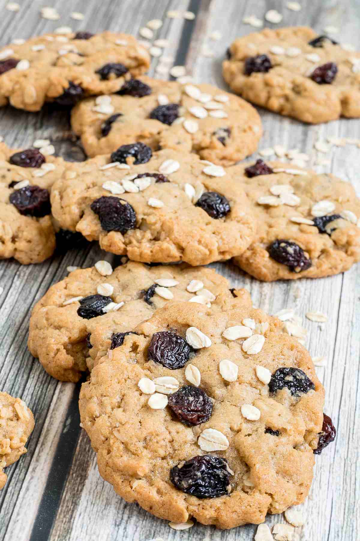 Lots of cookies with oats and raisins on a wooden surface. More oats are sprinkled around them.