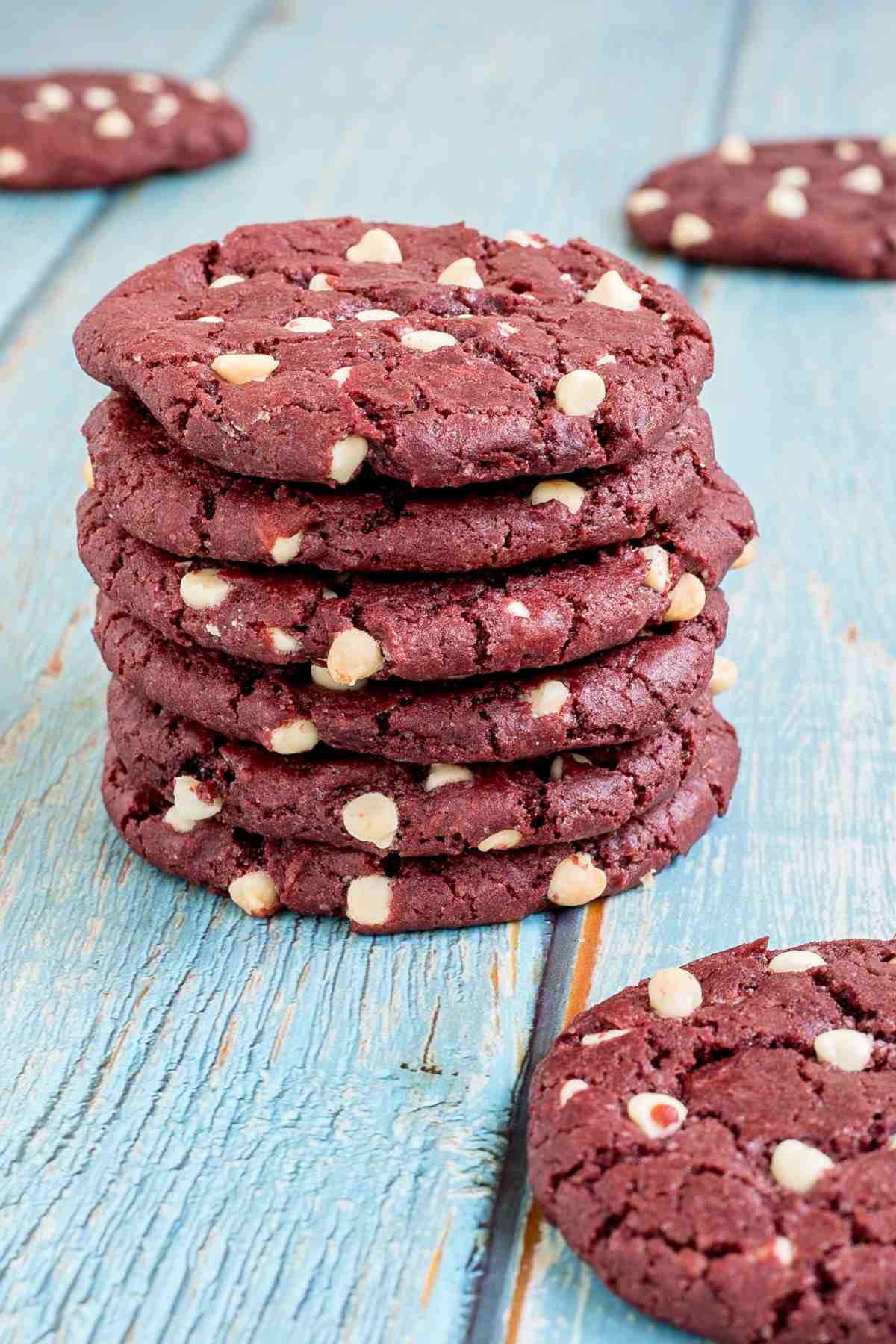 A stack of red velvet cookies with white chocolate chips on a light blue wooden surface.
