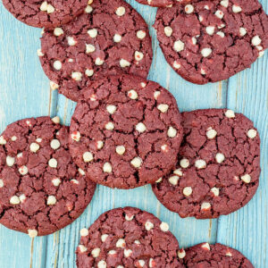 Lot of red velvet cookies with white chocolate chips on a light blue wooden surface.
