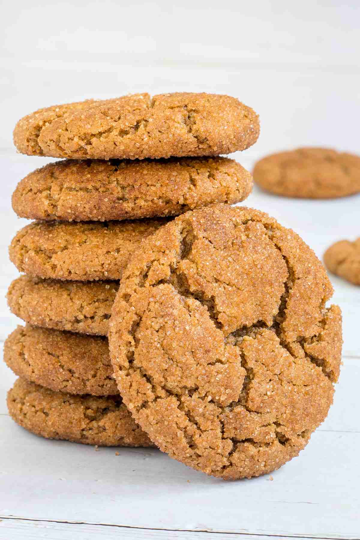 A stack of light brown cookies with crinkled top on a white wooden surface.