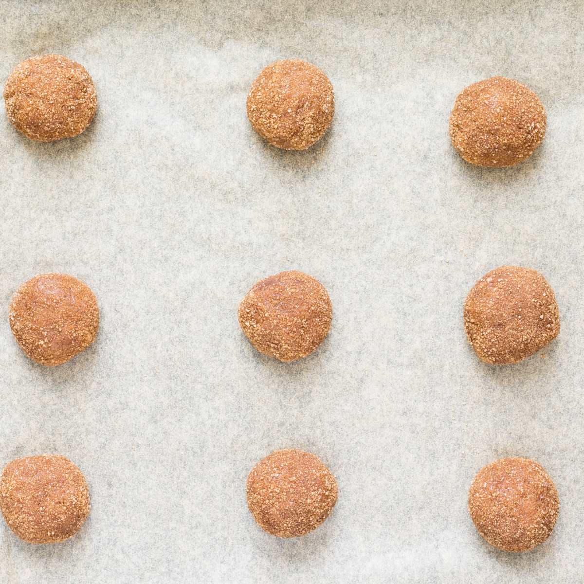 Small light brown uncooked cookie balls dusted in cinnamon sugar on parchment paper.