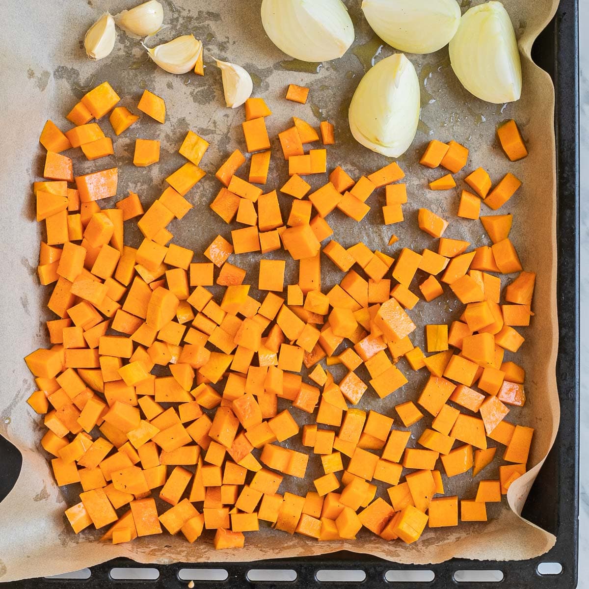 A baking sheet with onion wedges, garlic cloves, and diced butternut squash.