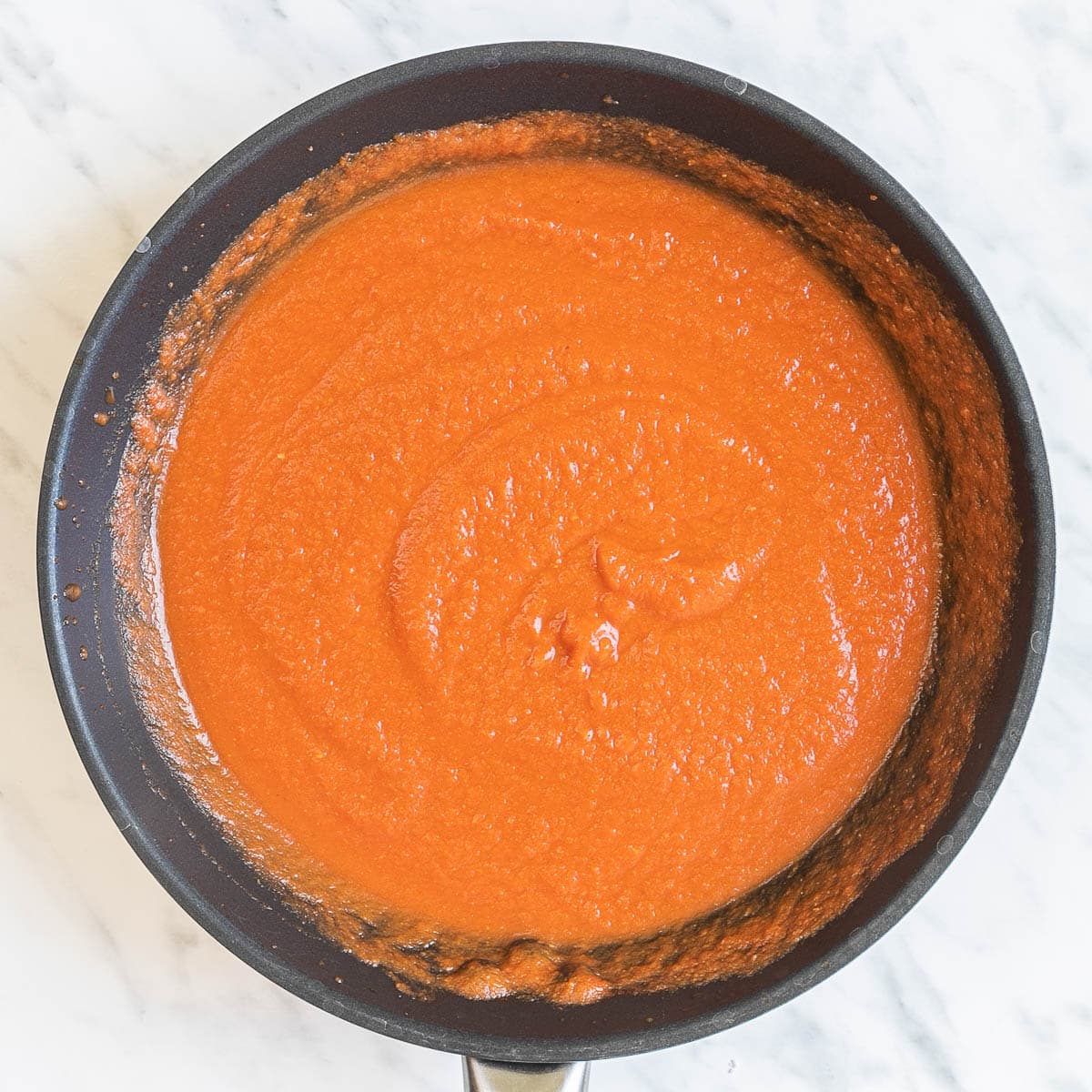 A thick red sauce in a black frying pan.