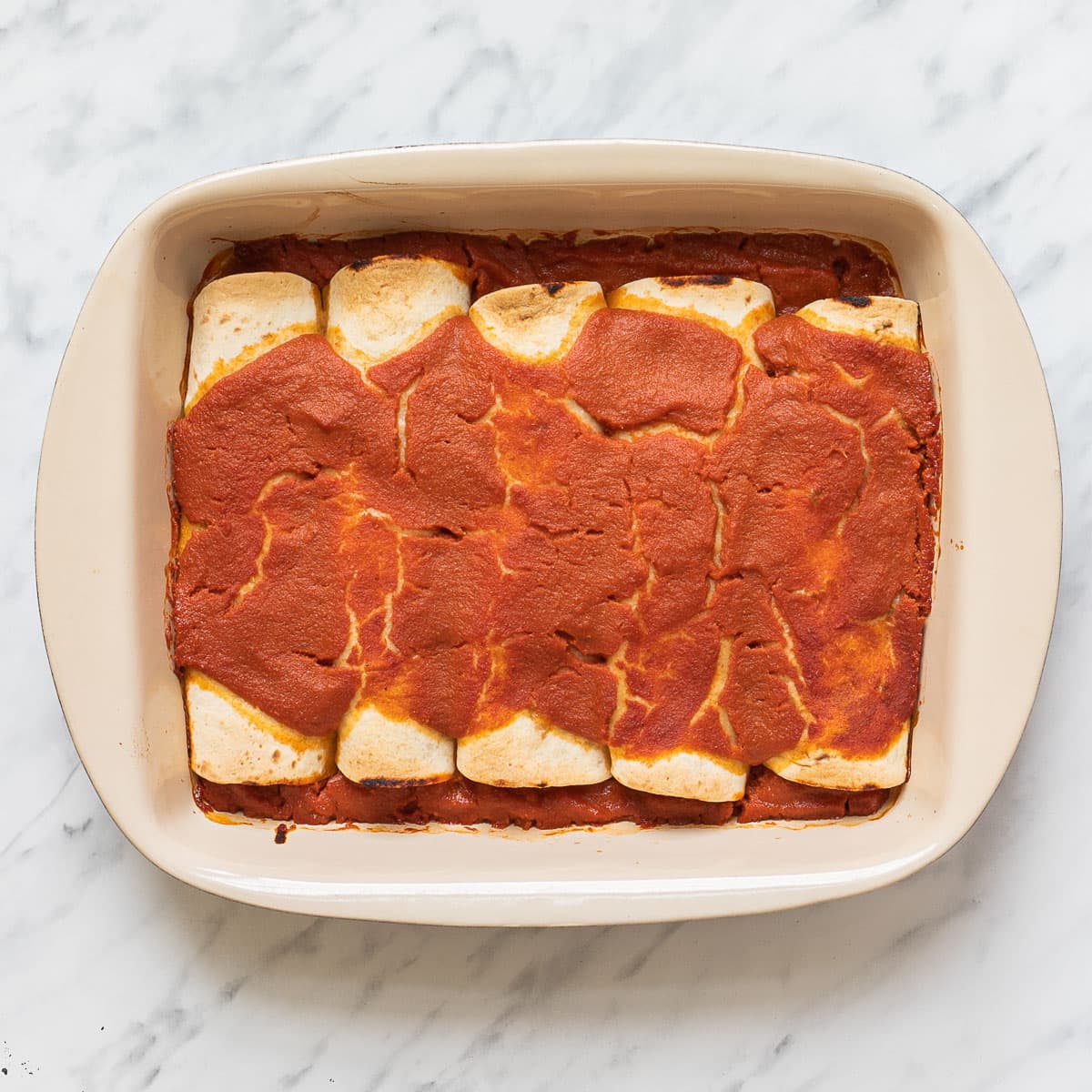 A casserole pan with rolled tortillas covered in red sauce.