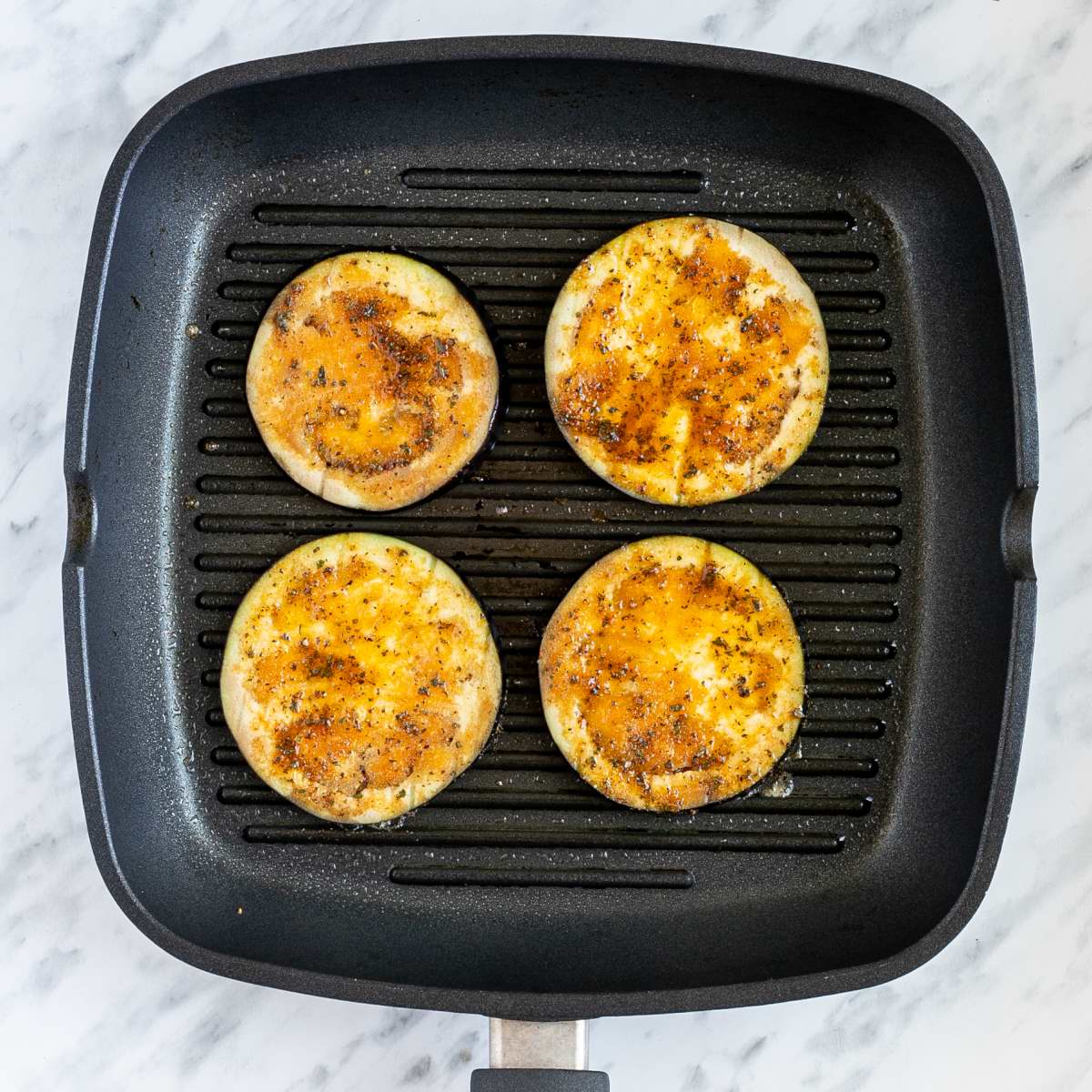 Grill pan with large marinated eggplant slices.
