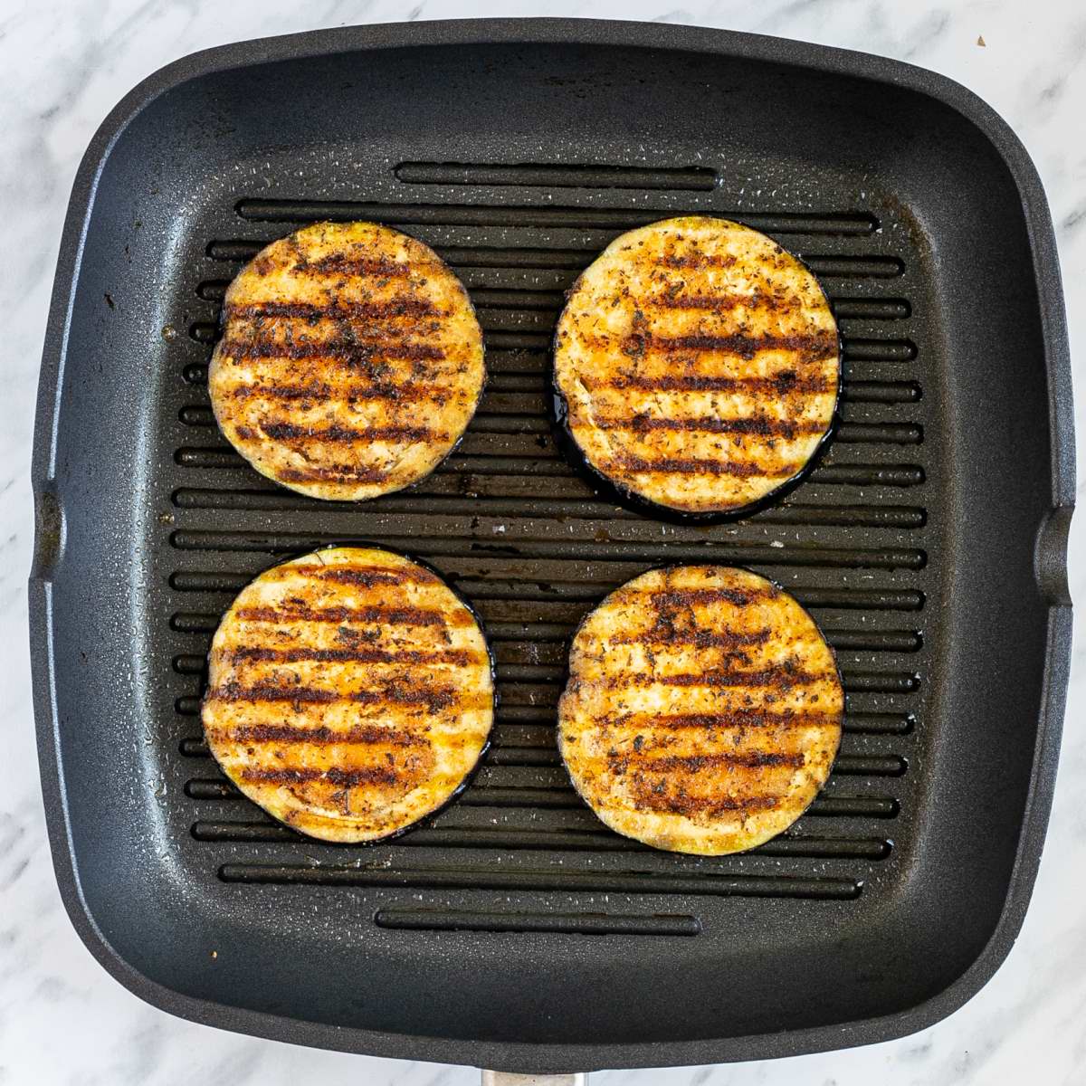 Grill pan with large marinated and charcoaled eggplant slices.