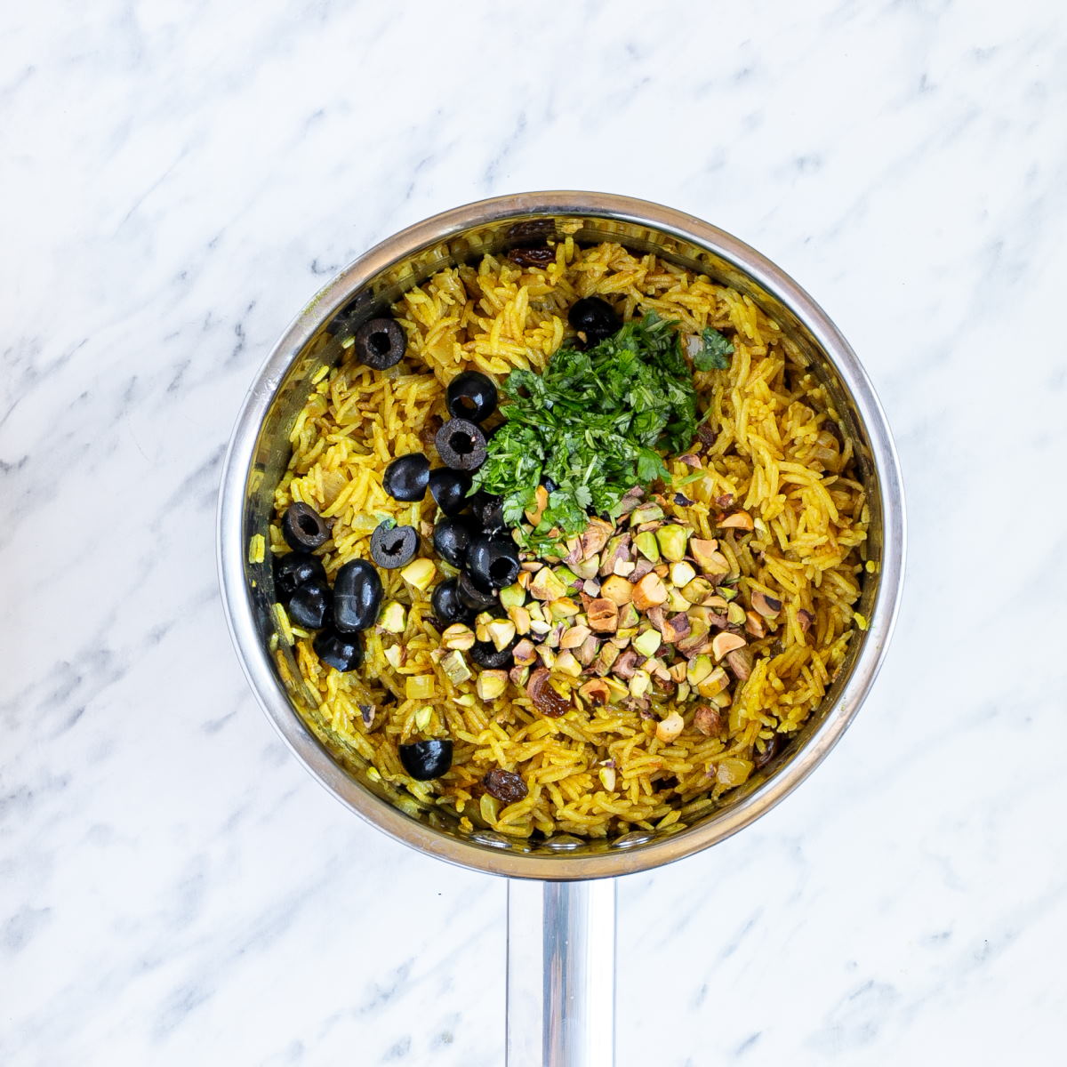 Pan with yellow rice topped with green herbs and chopped pistachios.