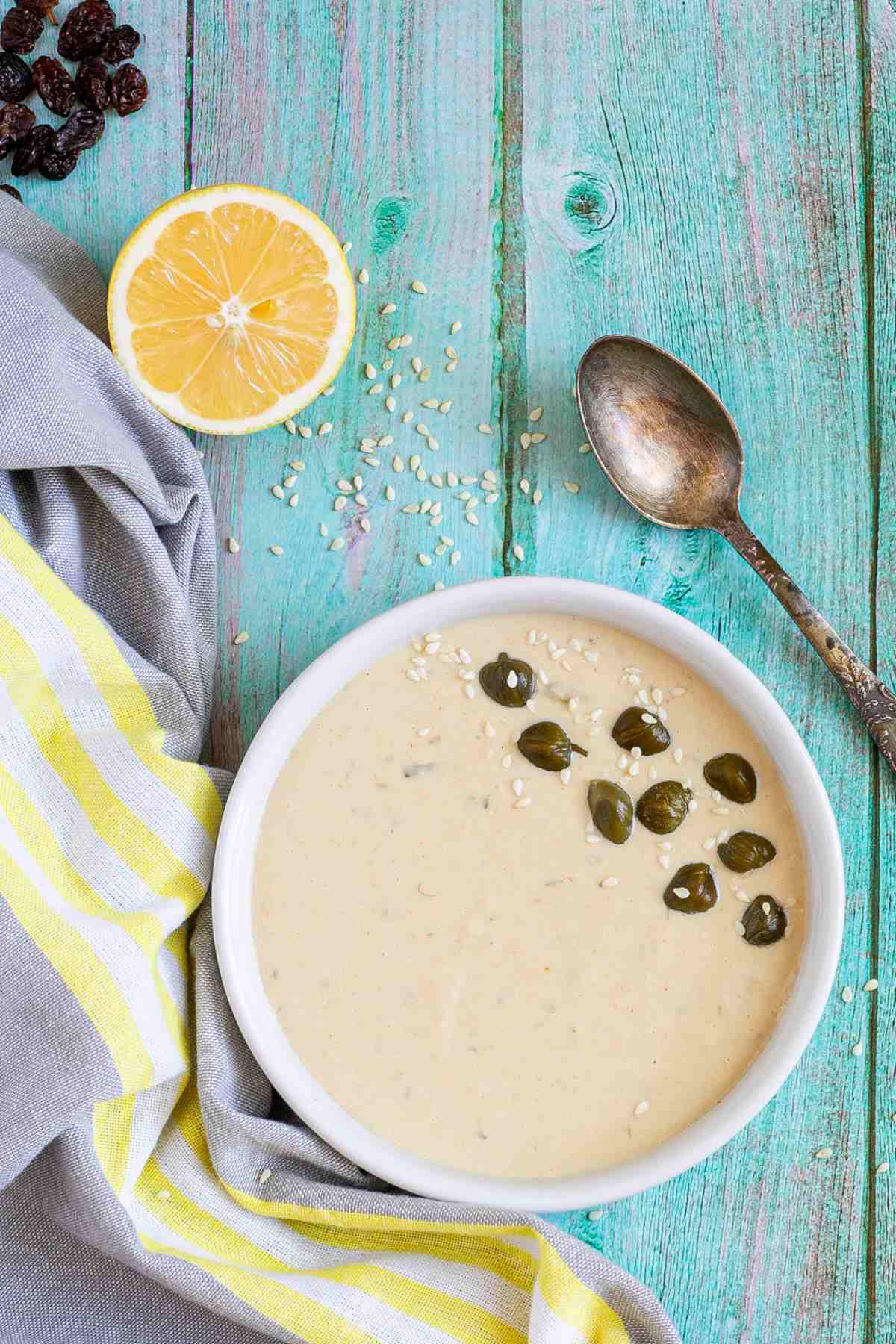 Small white bowl with a light brown thick sauce topped with sesame seeds and capers.