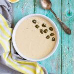 Small white bowl with a light brown thick sauce topped with sesame seeds and capers.