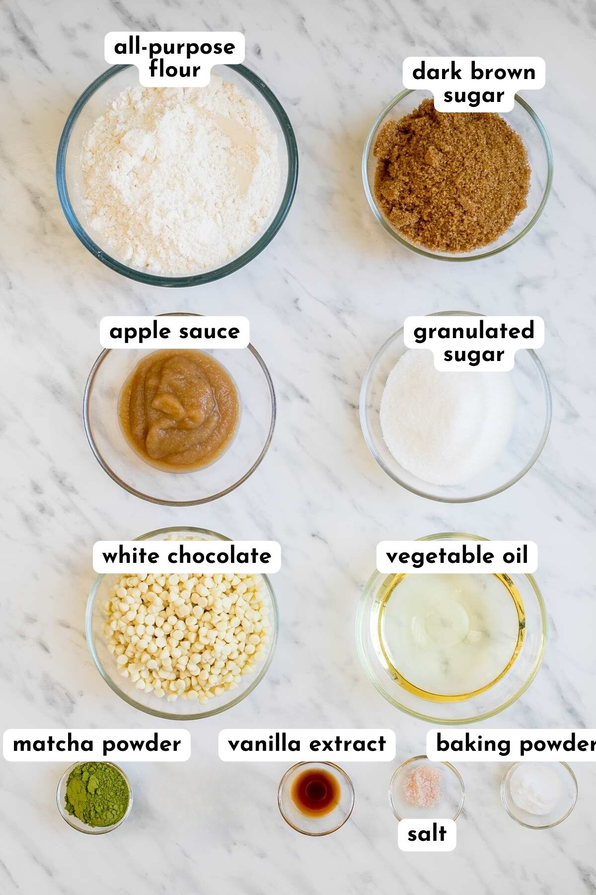 Ingredients of matcha cookies in small glass bowls like flour, sugar, white chocolate chips, green tea powder, apple sauce, oil, salt, baking soda.
