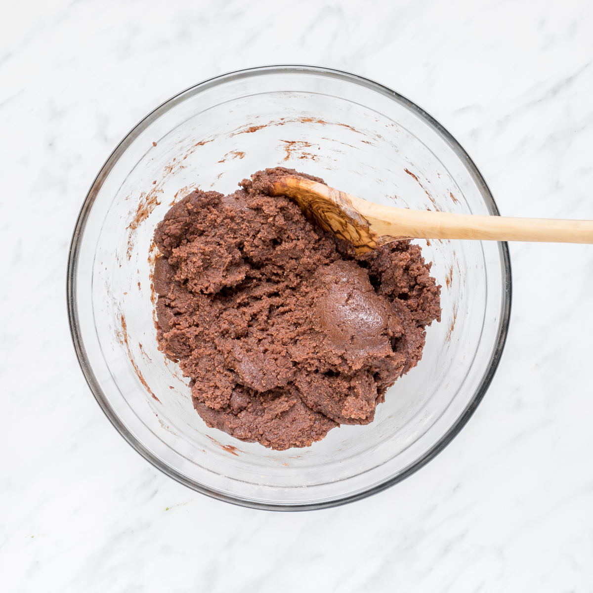 A glass bowl with brown cookie dough and a wooden spatula.