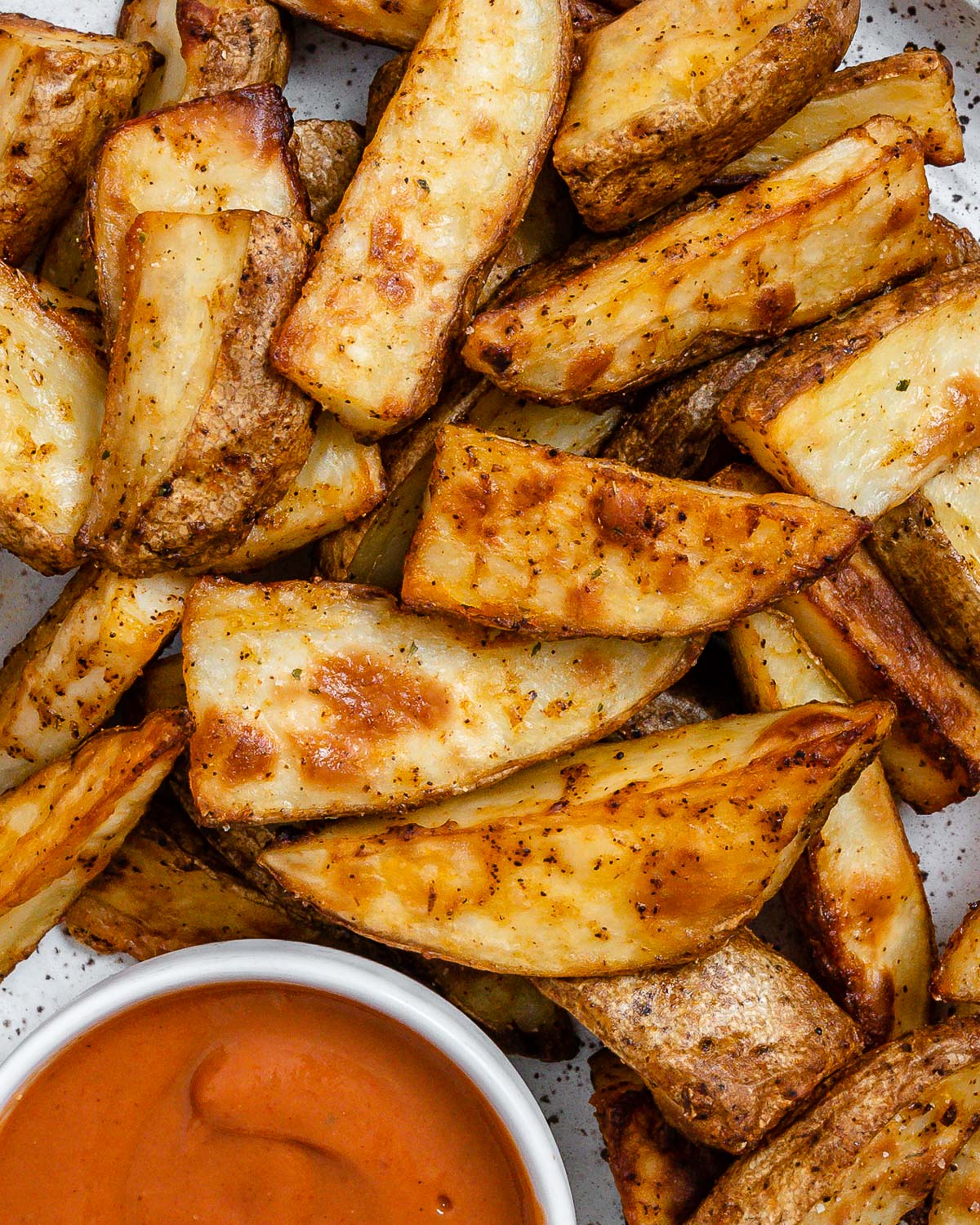 completed Air Fryer Potato Wedges plated on a white plate alongside a sauce.