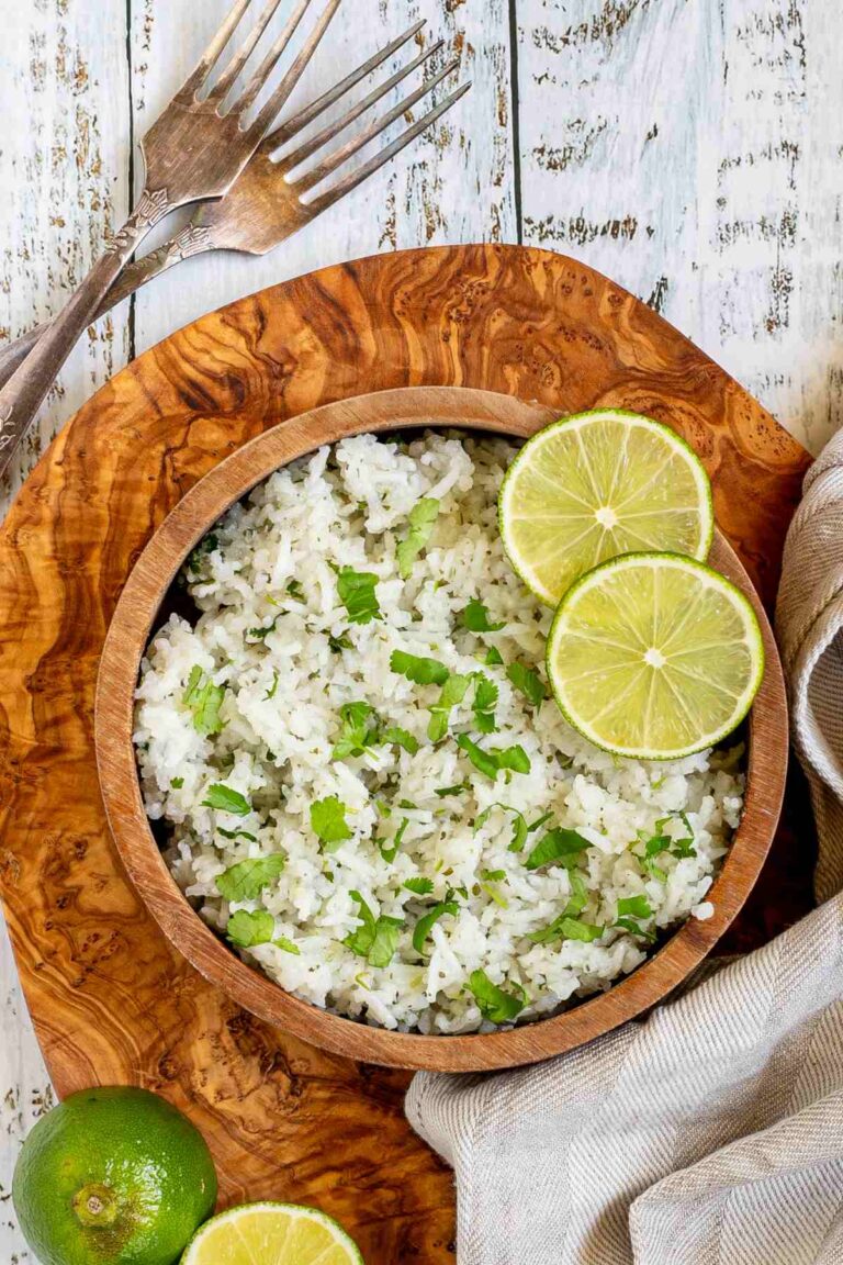 White rice with chopped cilantro and lime slices in a wooden bowl.