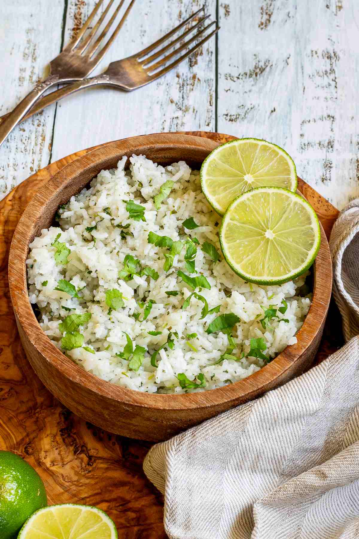White rice with chopped cilantro and lime slices in a wooden bowl.