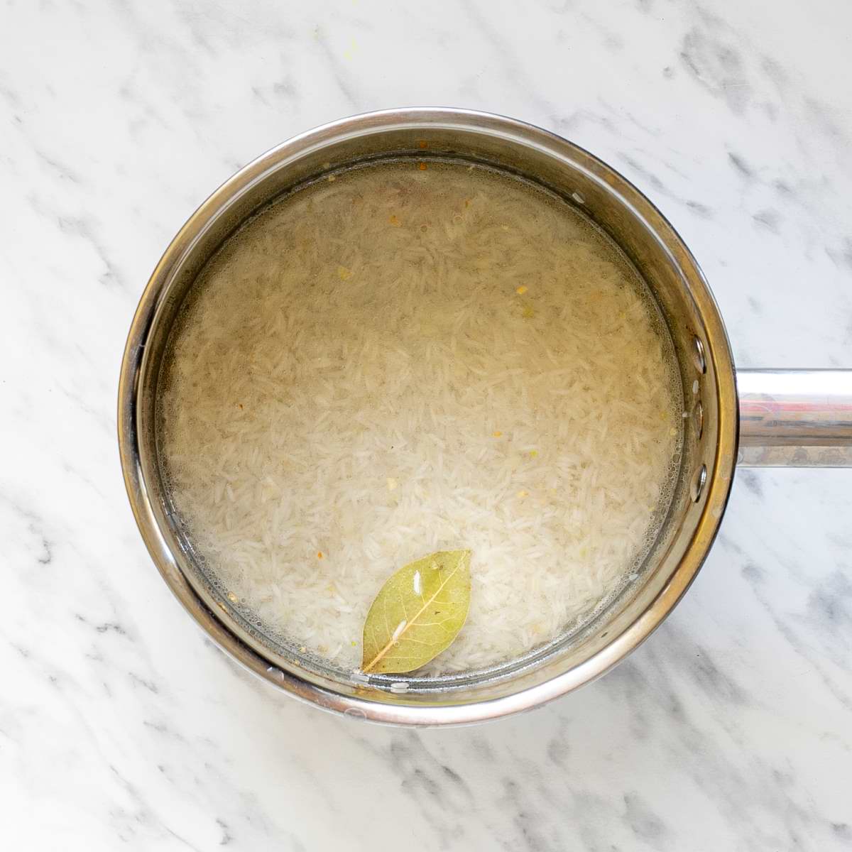 Small saucepan with white rice in water and a bay leaf.