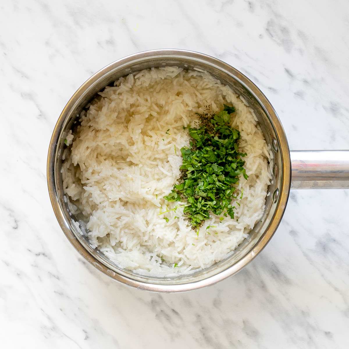 Small saucepan with fluffy white rice and a small heap of chopped cilantro.