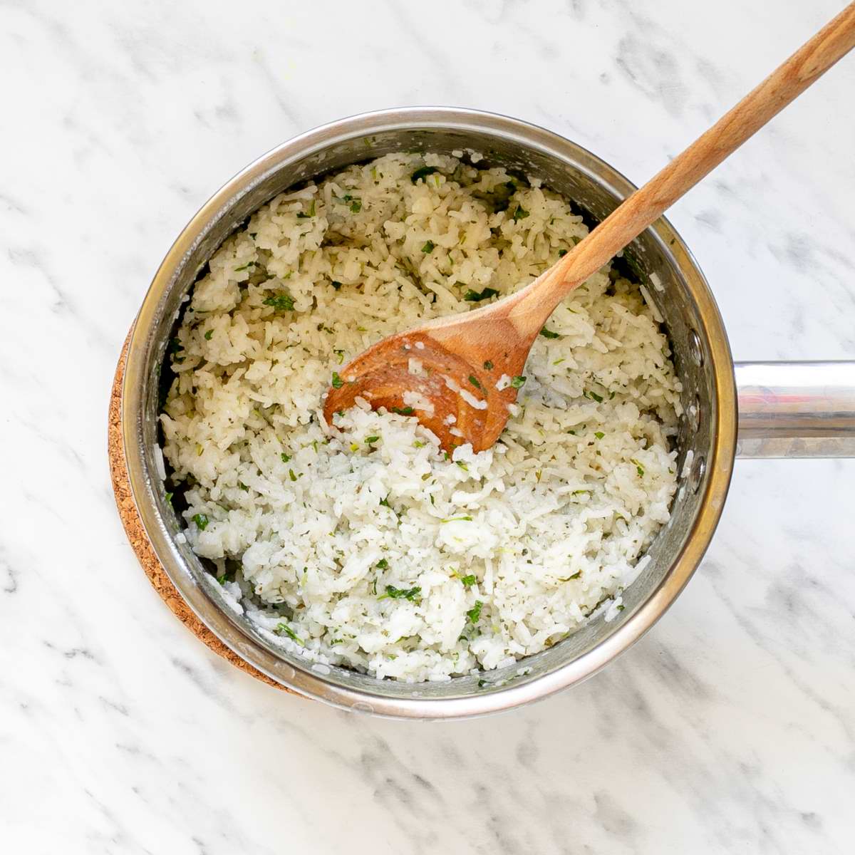 Small saucepan with white rice mixed with chopped green herbs.