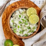 White rice with chopped cilantro and lime slices in a wooden bowl.
