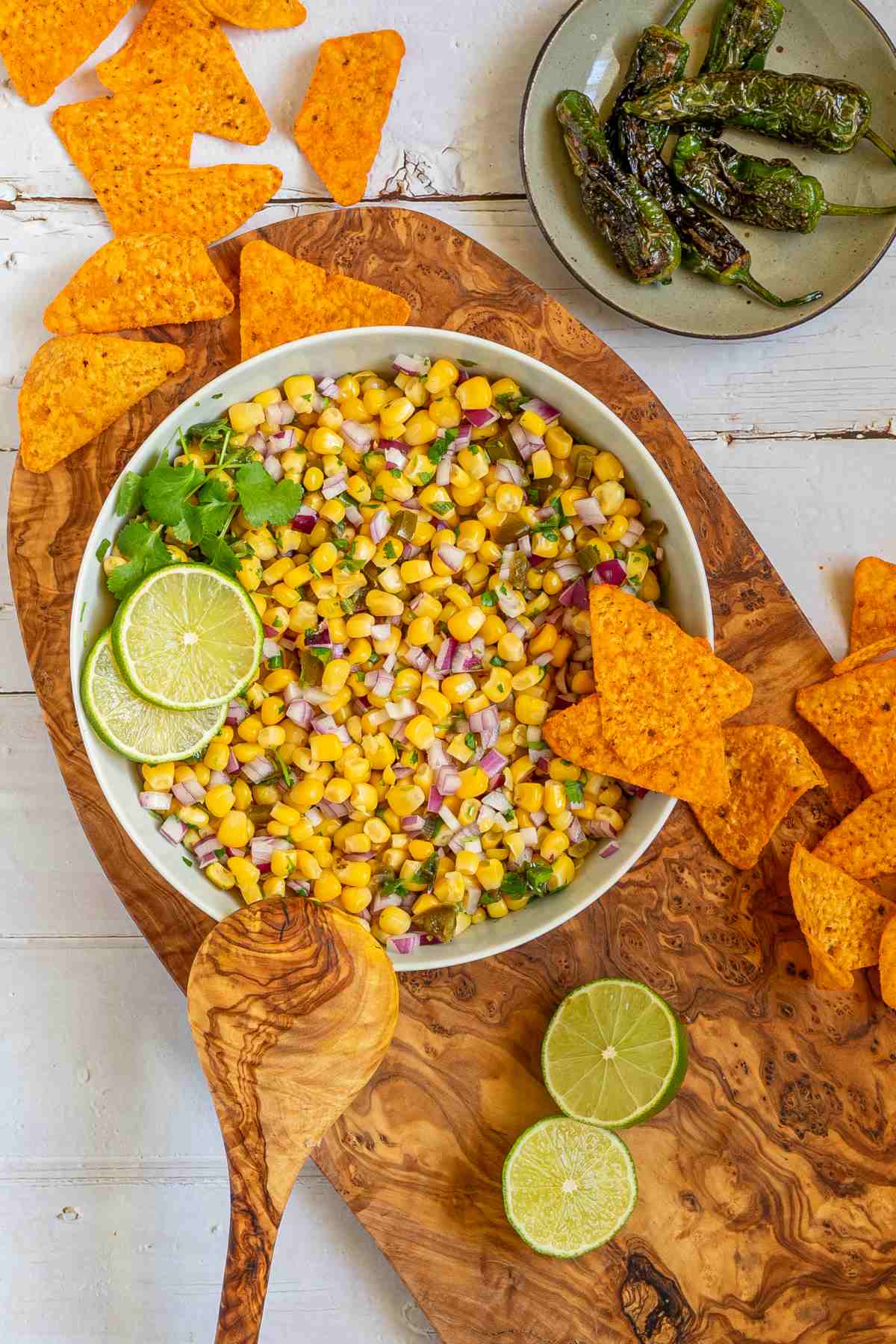 Corn salsa in a large white bowl with lime slices and nachos.