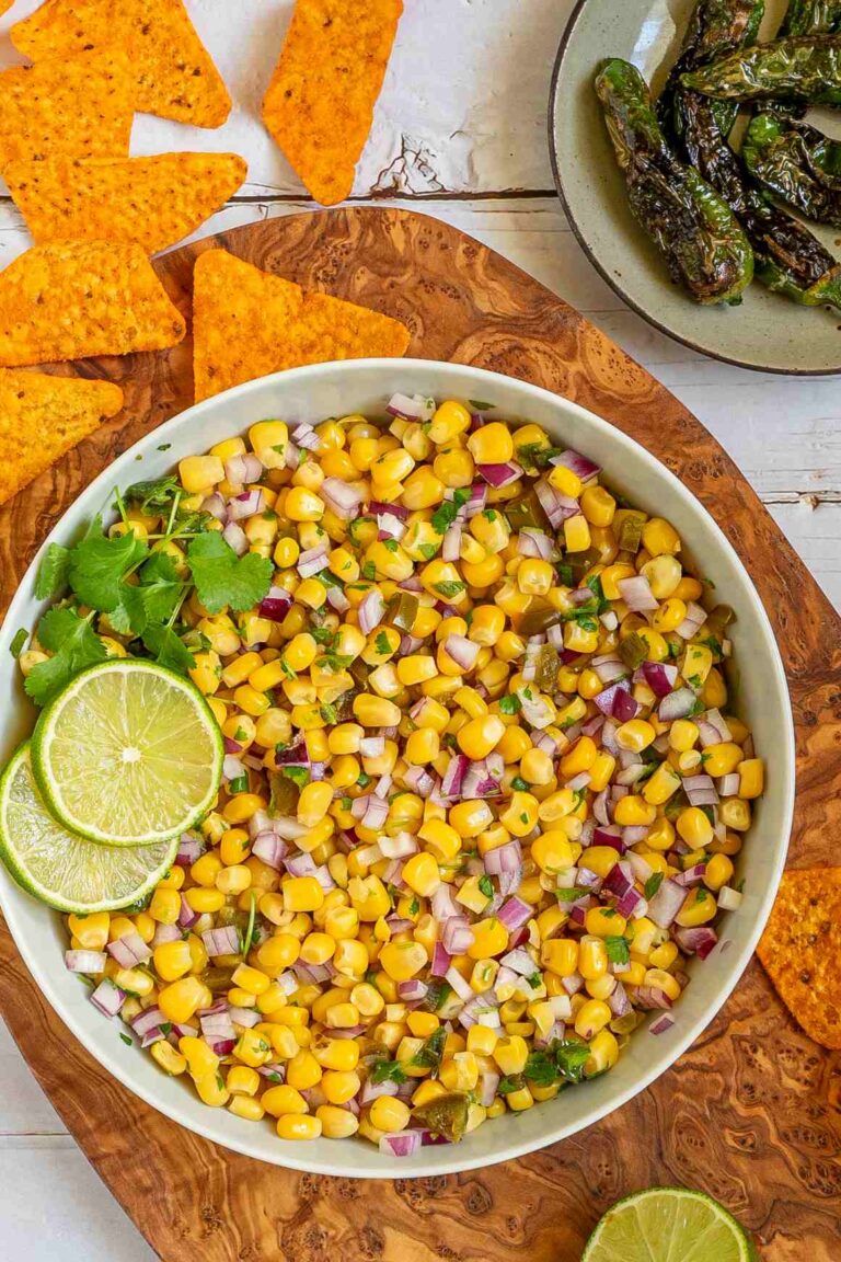 Corn salsa in a large white bowl with lime slices and nachos.