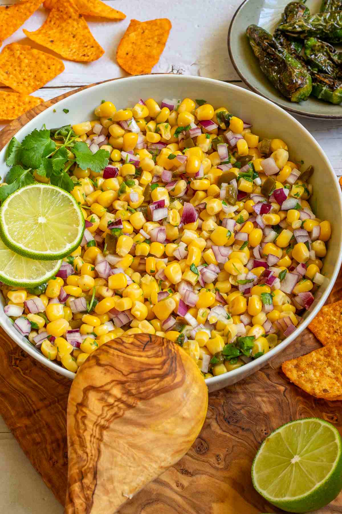 Corn salsa in a large white bowl with lime slices and nachos.