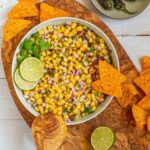 Corn salsa in a large white bowl with lime slices and nachos.