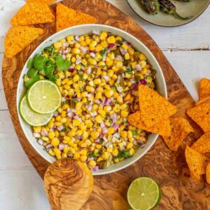 Corn salsa in a large white bowl with lime slices and nachos.